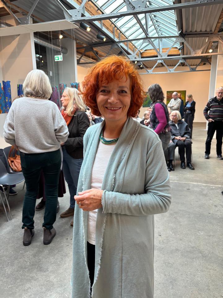 Isabelle Wiessler steht lächelnd in einer Galerie mit Kunstwerken im Hintergrund.