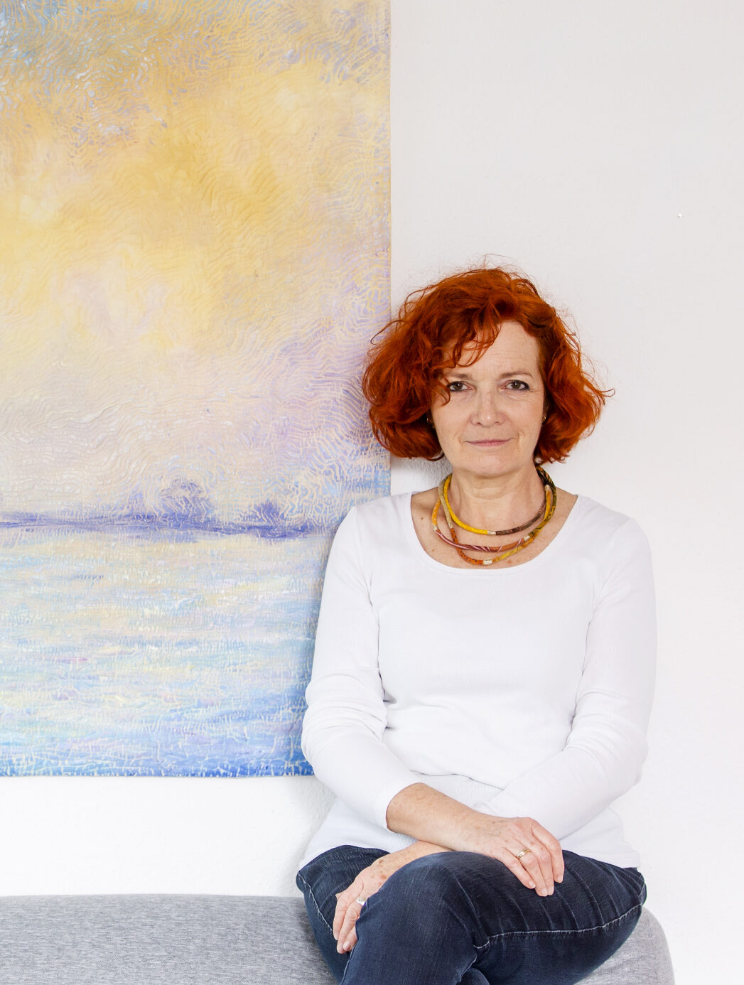 Porträt einer Frau (Isabelle Wiessler) mit roten Haaren und einem Kunstwerk im Hintergrund.