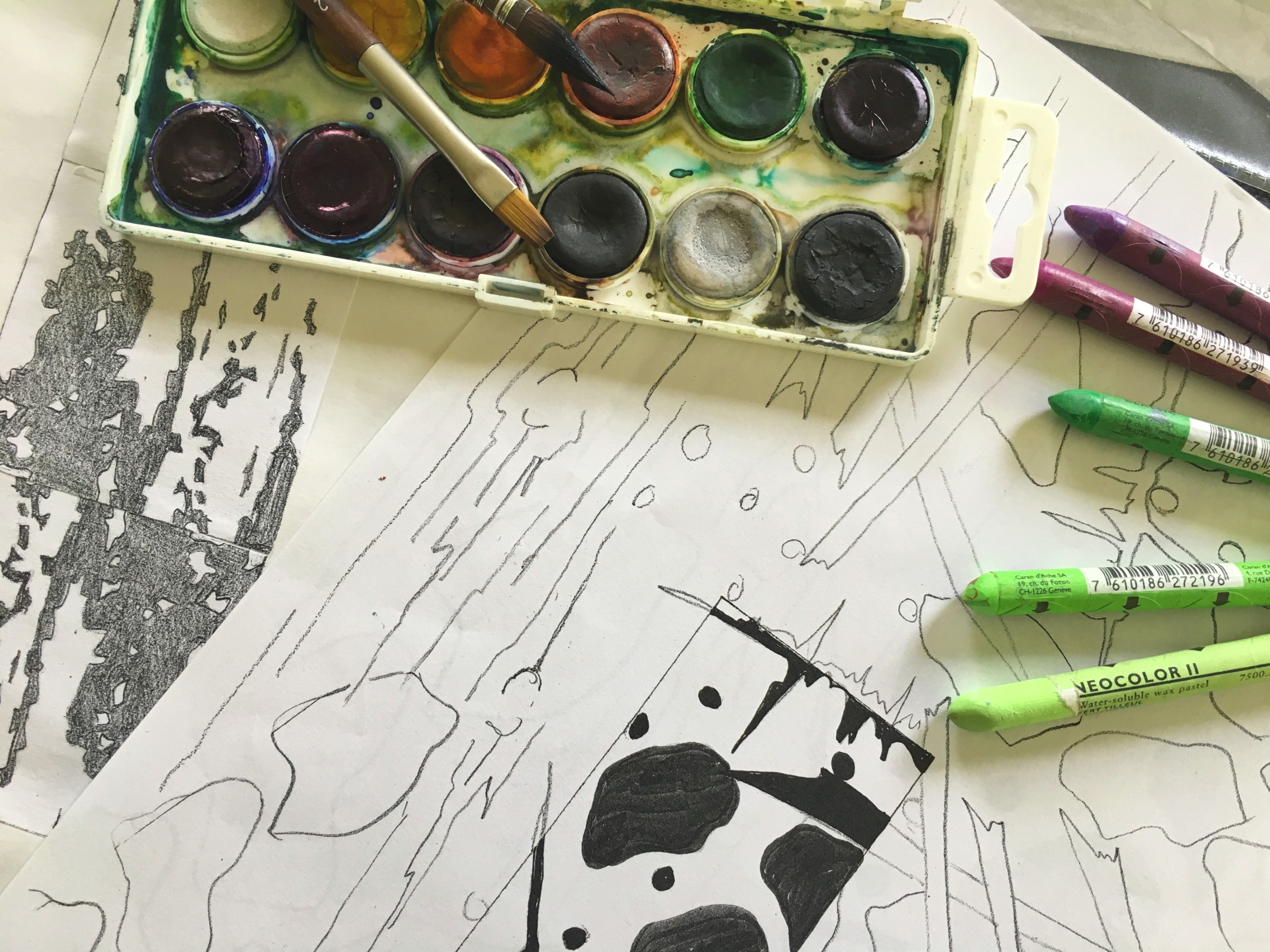 Künstlerischer Arbeitsprozess mit Farben und Materialien auf Tisch.