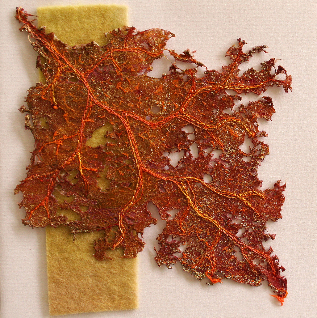 Ein kunstvoll gestaltetes, skelettiertes Blatt in Rostrot und Orange. Die Blattadern sind durch Stickerei oder Hitzebehandlung plastisch hervorgehoben, was dem Werk eine organische, fragile Struktur verleiht.