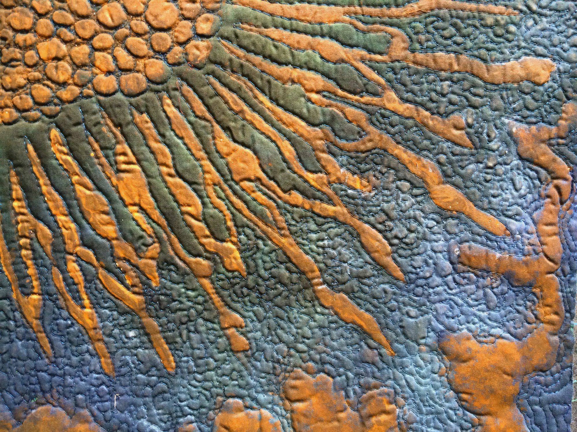 Nahaufnahme einer Textilarbeit in Grün- und Gelbtönen mit kreuzförmigen Stichen und plastischen, dunkelblauen Akzenten.