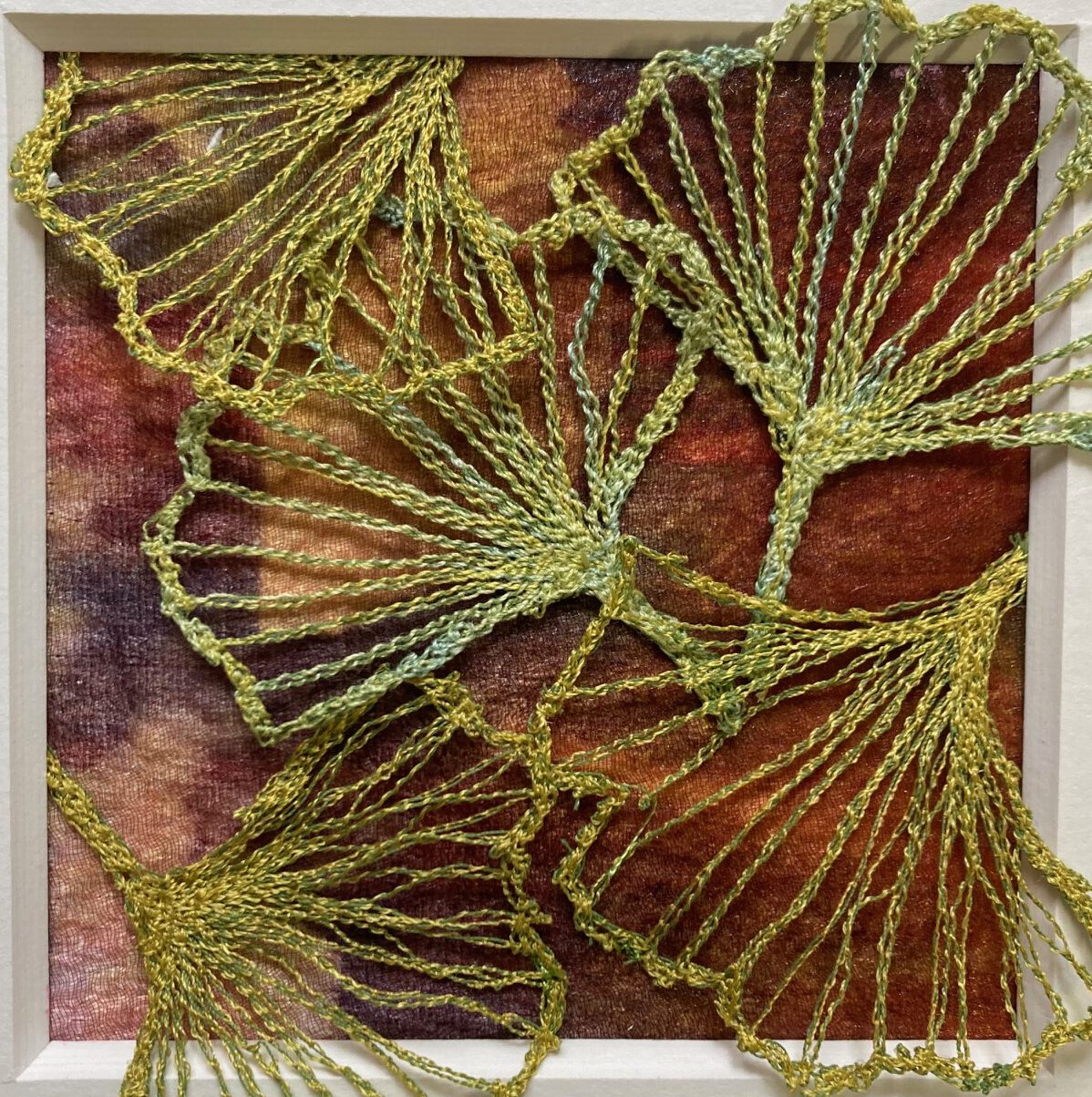 Filigrane, gold-grüne Blattumrisse (Ginkgo-Stil) aus feinem Garn auf einem dunkelrot-braun marmorierten Hintergrund.