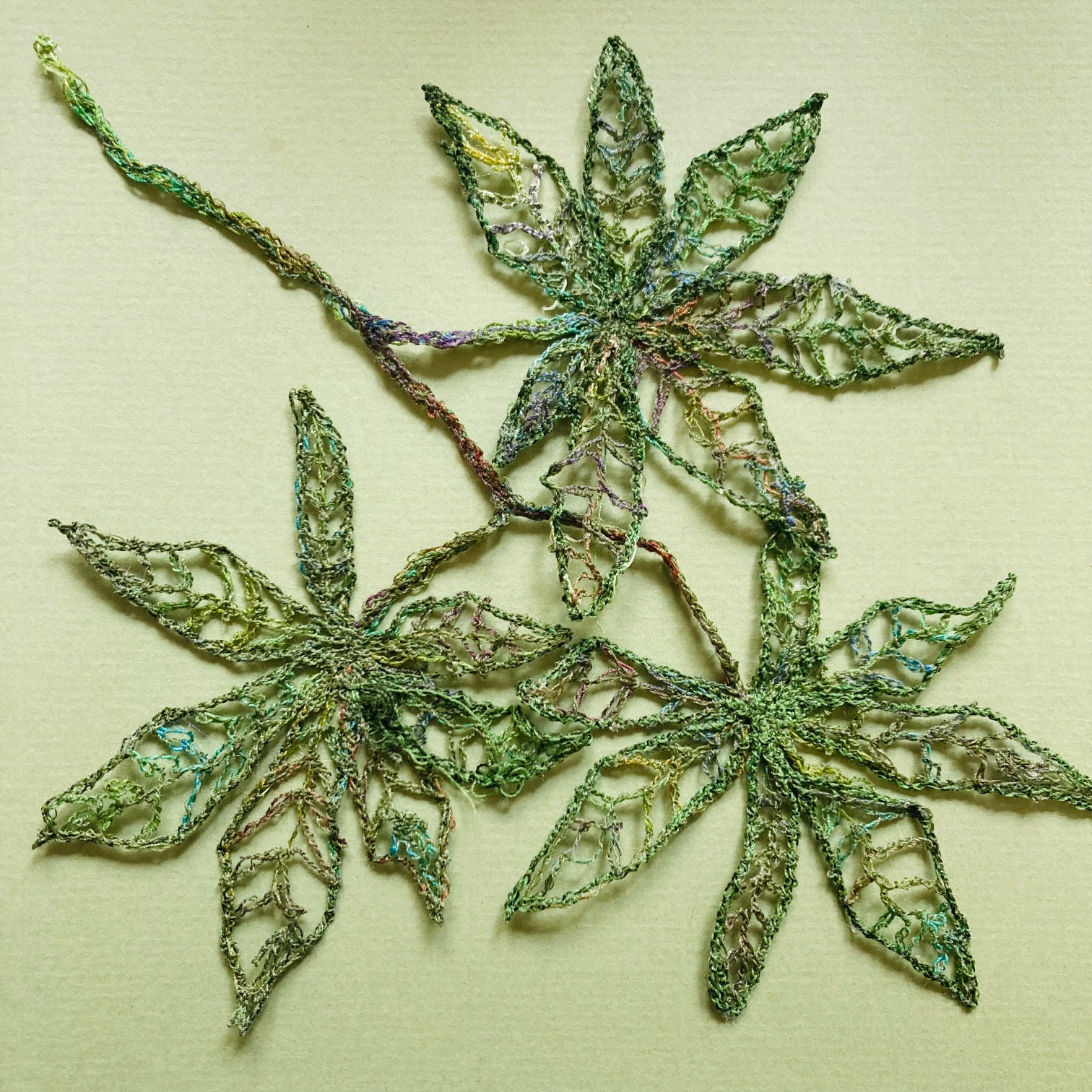Drei detailliert gestickte, grüne Blätter mit netzartiger Struktur auf hellem Grund.