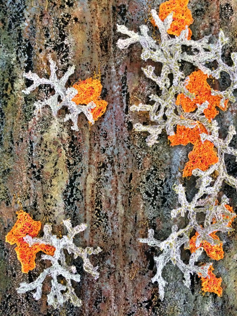 Sehr detailreiche Textilarbeit, die silbrig-graue und leuchtend orangefarbene Flechten auf einem dunklen Untergrund imitiert.