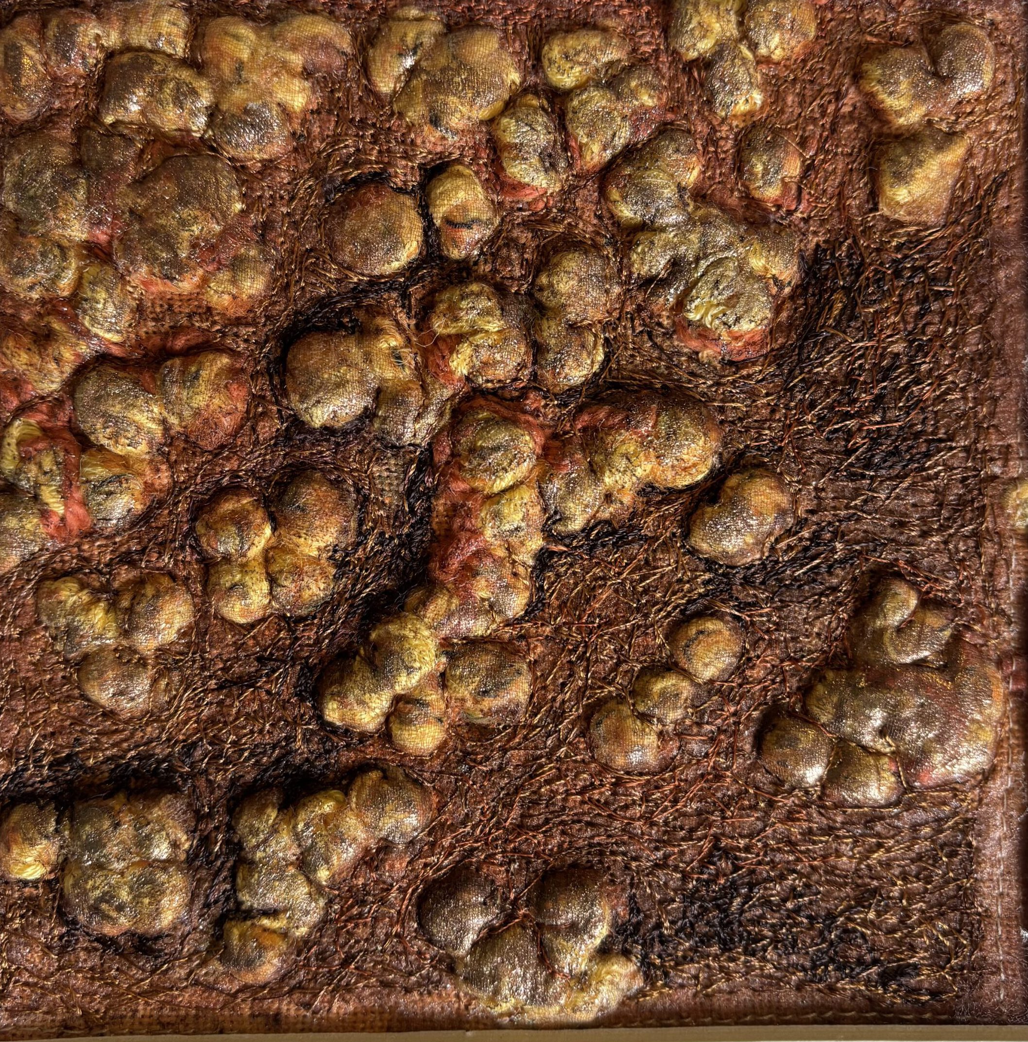 Eine stark strukturierte, organische Textiloberfläche in Erdtönen, die an Baumrinde oder kleine Knollen erinnert.